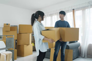 Asyalı genç mutlu evli çift yeni evlerine ya da gayrimenkullerine taşınıyor. Çekici romantik bir erkek ve kadın, içinde mutluluk ve sevgi olan kutular taşır. Aile taşınma konsepti.