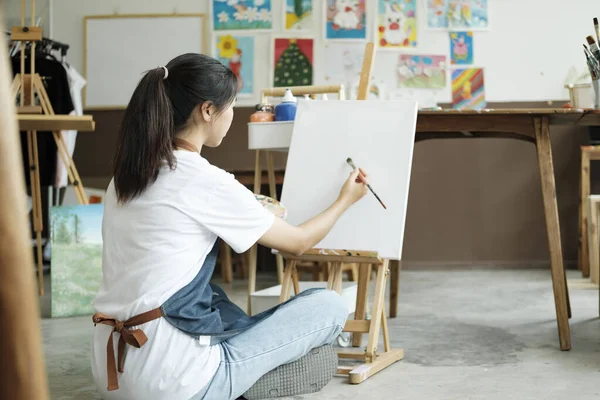 Young female artist sketches or paints her drawing on canvas in a studio workshop. A teenage girl who likes art and drawing is taking time to create her watercolors on canvas with great intention