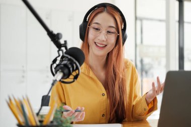 Canlı yayına ev sahipliği yapan neşeli kadın stüdyoda profesyonel mikrofon kullanarak seyircilerle iletişim kuruyor..