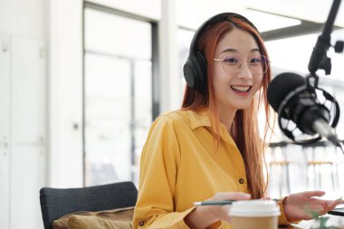 Canlı yayına ev sahipliği yapan neşeli kadın stüdyoda profesyonel mikrofon kullanarak seyircilerle iletişim kuruyor..