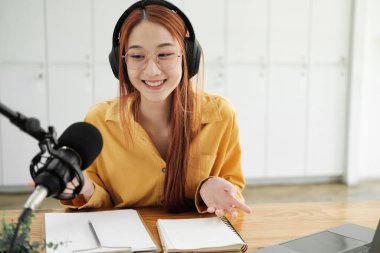 Canlı yayına ev sahipliği yapan neşeli kadın stüdyoda profesyonel mikrofon kullanarak seyircilerle iletişim kuruyor..