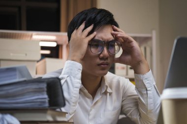 Masaüstü bilgisayarını kullanan Asyalı genç ve yorgun iş adamı ofiste gece boyunca fazla mesai yapıyor..