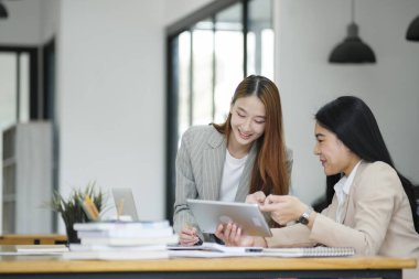 Ofisteki kadın ayakta duruyor ve yeni bir çalışana ders veriyor. Tablet ekranında gösterilen çalışma biçimini tanımlar.