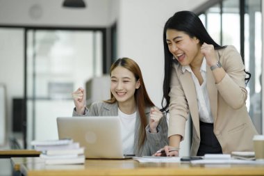 İki mest olmuş iş kadını iş yerinde başarılı bir anı bir dizüstü bilgisayar ve belgeler ile kutluyorlar...