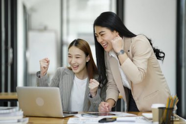 İki mest olmuş iş kadını iş yerinde başarılı bir anı bir dizüstü bilgisayar ve belgeler ile kutluyorlar...
