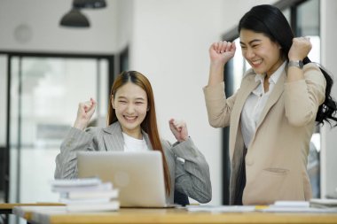 İki mest olmuş iş kadını iş yerinde başarılı bir anı bir dizüstü bilgisayar ve belgeler ile kutluyorlar...