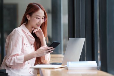 Evde dizüstü bilgisayarla çalışırken akıllı telefon kullanan çok çekici bir kadın. Çevrimiçi iletişim kavramı.