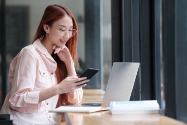 Evde dizüstü bilgisayarla çalışırken akıllı telefon kullanan çok çekici bir kadın. Çevrimiçi iletişim kavramı.