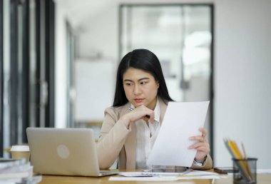Elinde parlak bir ofis ortamında dizüstü bilgisayarla çalışan odaklanmış bir iş kadını...