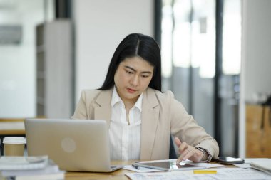 Elinde parlak bir ofis ortamında dizüstü bilgisayarla çalışan odaklanmış bir iş kadını...