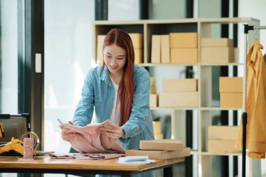 Gülümseyen bayan girişimci atölyesinde nakliye için kıyafet paketliyor..