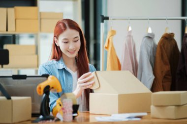 Gülümseyen bayan girişimci atölyesinde nakliye için kıyafet paketliyor..