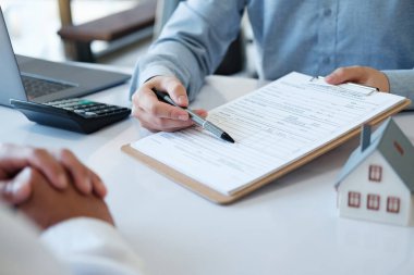 Bir emlakçı bir kalemle kredi sözleşmesini işaret ediyor. Belgeyi imzalamayı kabul eden müşterilere konut satın alma, kiralama veya yatırım yapma olanağı sağlamak.