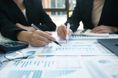 İki kadın bir masada bir sürü kağıt ve kalemle oturuyorlar. Birlikte bir proje üzerinde çalışıyorlar.