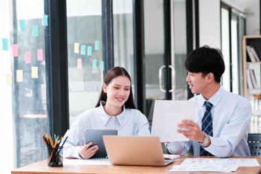 Modern ofis ortamında dizüstü bilgisayarda evrak ve dijital içeriği tartışan iki profesyonel meslektaş..