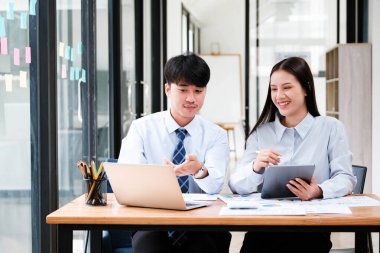 Şirket büyüme stratejisi için dijital ve kağıt veri analizi konusunda ofis masasında tartışan Asyalı iş arkadaşları.