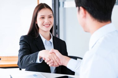 A young businesswoman smiles while shaking hands, making a positive impression during a professional meeting. clipart
