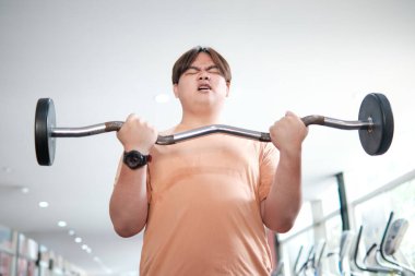 Kilolu bir adam spor salonunda halter kaldırıyor. Egzersizinde gayret ve kararlılık gösteriyor..