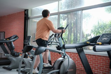 Spor salonunda eliptik bir makine üzerinde egzersiz yapan kilolu bir adam..