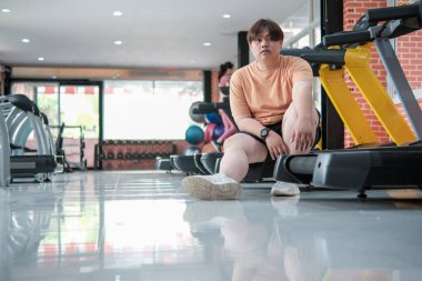 Aşırı egzersizden sonra kilolu bir adam spor salonunda oturup dinleniyor..