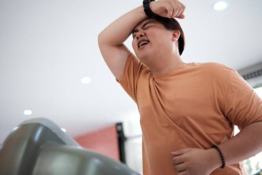 Spor salonunda koşu bandında koşan şişman bir adam alnından ter siliyor..