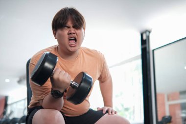 Bir adam ağırlık kaldırıyor ve çok sinirli bir ruh hali içinde. Turuncu bir gömlek ve siyah bir şort giyiyor.