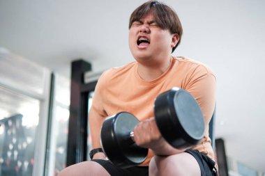 Bir adam ağırlık kaldırıyor ve çok sinirli bir ruh hali içinde. Turuncu bir gömlek ve siyah bir şort giyiyor.