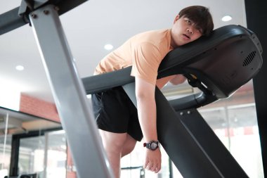Spor salonundaki koşu bandında yatan bir adam. Bir saat takıyor ve çok yorgun.