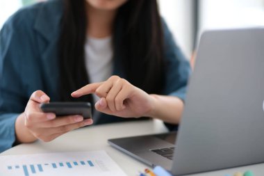 Bir kadın aynı anda hem cep telefonu hem de laptop kullanıyor. Telefondaki bir şeyi işaret ediyor ve dizüstü bilgisayara bakıyor. Sahne birden fazla iş yaptığını gösteriyor.