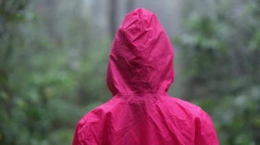 Pembe yağmurluk giyen biri bir ormanda duruyor. Biri gökyüzüne bakıyor ve yağmurluk ıslanmış.