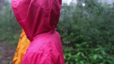 Yağmurluk ve sırt çantası giyen iki kişi bir ormanda duruyor. Bir tanesi gökyüzüne bakıyor.