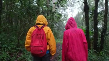 İki kişi ormanda yürüyor, biri sarı ceketli, diğeri pembe ceketli.