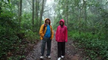 Biri sarı ceketli, diğeri de pembe ceketli iki kişi ormanda dikiliyorlar.