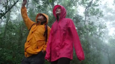 İki kişi ormanda yürüyor, biri sarı ceketli, diğeri pembe ceketli.