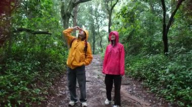 Biri sarı ceketli, diğeri de pembe ceketli iki kişi ormanda dikiliyorlar.