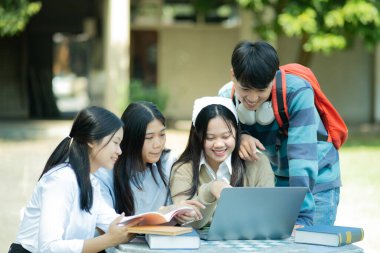 Bir grup üniversite öğrencisi kampüste birlikte okuyorlar, bir dizüstü bilgisayar ve kitapları ortak bir ortamda kullanıyorlar..