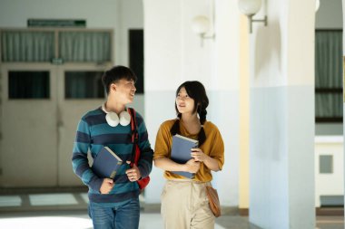 Bir grup üniversite öğrencisi kampüs koridorunda birlikte yürüyor, gülümsüyor ve kitap taşıyor, gündelik sohbetlere dalıyorlar..