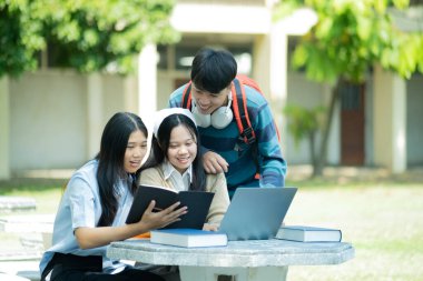 Bir grup üniversite öğrencisi kampüste birlikte okuyorlar, bir dizüstü bilgisayar ve kitapları ortak bir ortamda kullanıyorlar..