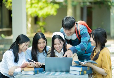 Bir grup üniversite öğrencisi kampüste birlikte okuyorlar, bir dizüstü bilgisayar ve kitapları ortak bir ortamda kullanıyorlar..