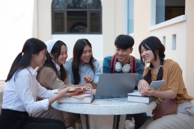 Bir grup üniversite öğrencisi kampüste birlikte okuyorlar, bir dizüstü bilgisayar ve kitapları ortak bir ortamda kullanıyorlar..