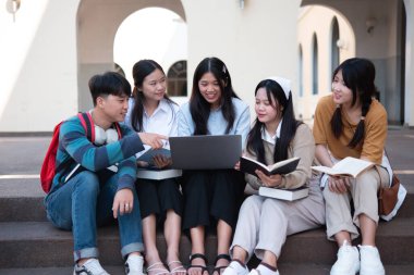 Bir grup üniversite öğrencisi kampüste birlikte okuyorlar, bir dizüstü bilgisayar ve kitapları ortak bir ortamda kullanıyorlar..