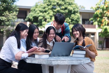 Bir grup üniversite öğrencisi kampüste birlikte okuyorlar, bir dizüstü bilgisayar ve kitapları ortak bir ortamda kullanıyorlar..