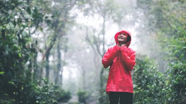 Kırmızı yağmurluklu genç bir kadın yemyeşil, yemyeşil bir ormanda derin bir nefes alıyor ve doğal çevreyi kucaklıyor..