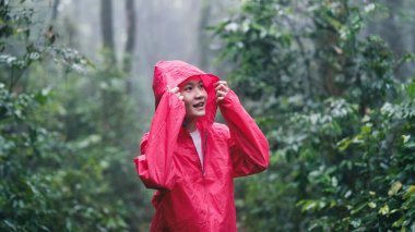 Kırmızı yağmurluk giyen bir kadın, sisli bir günde temiz havanın ve doğal güzelliğin tadını çıkarırken neşeyle gülümser..