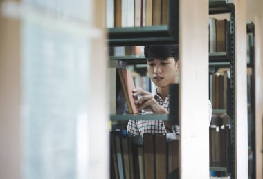 Bir üniversite öğrencisi ya da lise öğrencisi kütüphane rafından ders çalışmak, araştırma yapmak ya da ödev yapmak için kitap seçer..