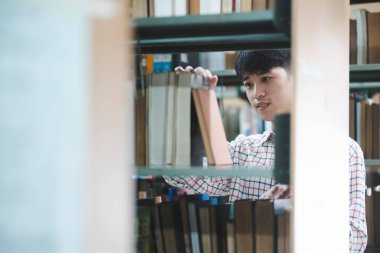 Bir üniversite öğrencisi ya da lise öğrencisi kütüphane rafından ders çalışmak, araştırma yapmak ya da ödev yapmak için kitap seçer..