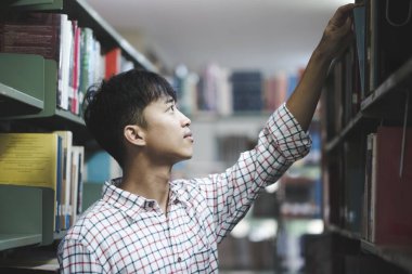 Bir üniversite öğrencisi ya da lise öğrencisi kütüphane rafından ders çalışmak, araştırma yapmak ya da ödev yapmak için kitap seçer..