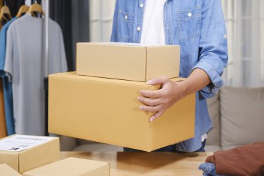 Kendine güvenen Asyalı genç adam perakende satıcısı, girişimci, çevrimiçi mağaza teslimatçısı küçük işletme sahibi teslimat deposunda paketle duran kameraya bakıyor..