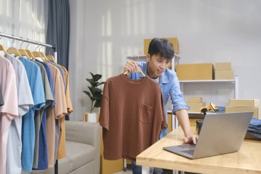 Genç girişimci canlı yayında giyim ürünleri değerlendirmesi yapıyor. Seyircilerine akıllı telefon ve zil ışığı kullanarak tişört sergiliyor..