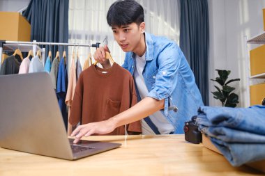 Genç girişimci canlı yayında giyim ürünleri değerlendirmesi yapıyor. Seyircilerine akıllı telefon ve zil ışığı kullanarak tişört sergiliyor..